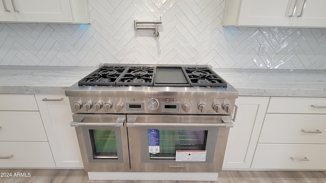 kitchen with light stone counters, white cabinets, light hardwood / wood-style flooring, range with two ovens, and backsplash