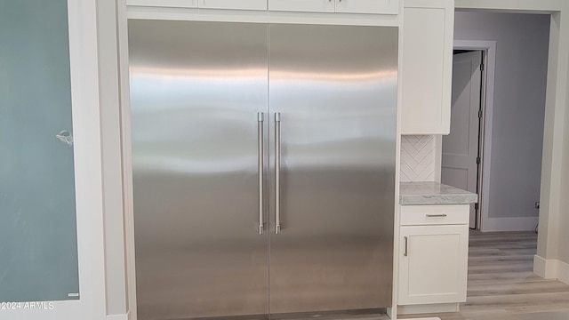 interior details featuring stainless steel built in fridge, tasteful backsplash, white cabinetry, light stone countertops, and light hardwood / wood-style floors