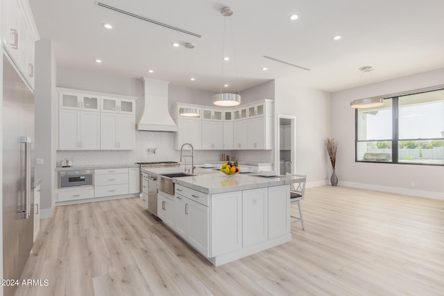 kitchen with light hardwood / wood-style flooring, white cabinets, a kitchen island with sink, and premium range hood