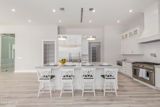 kitchen with a large island, light wood-type flooring, pendant lighting, high quality appliances, and premium range hood