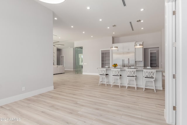 kitchen with white cabinets, kitchen peninsula, a breakfast bar area, light wood-type flooring, and sink