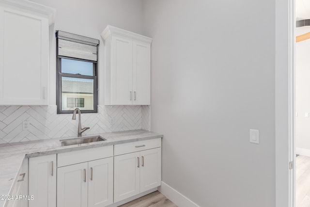 kitchen with light wood-type flooring, light stone counters, sink, white cabinetry, and backsplash