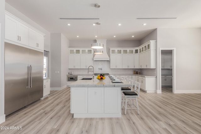 kitchen with an island with sink, premium range hood, sink, appliances with stainless steel finishes, and light hardwood / wood-style floors