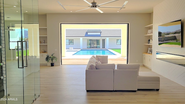 living room featuring built in shelves, light hardwood / wood-style flooring, and ceiling fan