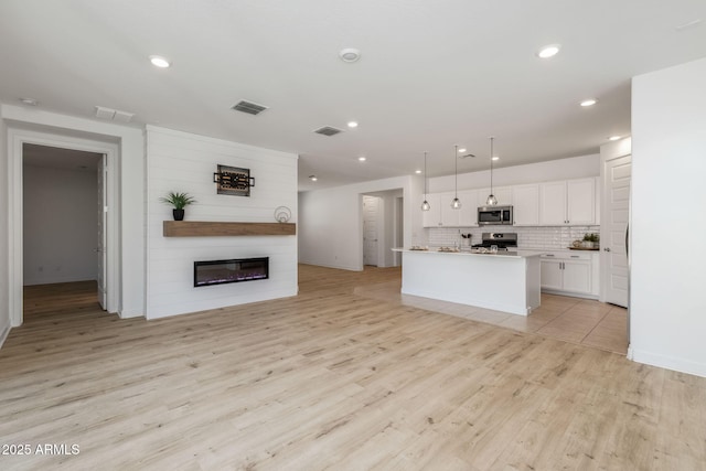 kitchen with visible vents, backsplash, open floor plan, stainless steel appliances, and white cabinetry