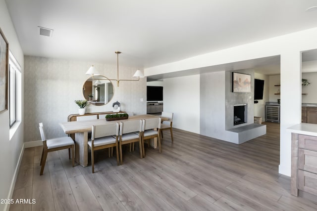 dining area featuring a large fireplace, wine cooler, hardwood / wood-style floors, and a chandelier