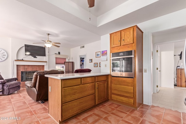 kitchen with kitchen peninsula, ceiling fan, oven, and a tiled fireplace