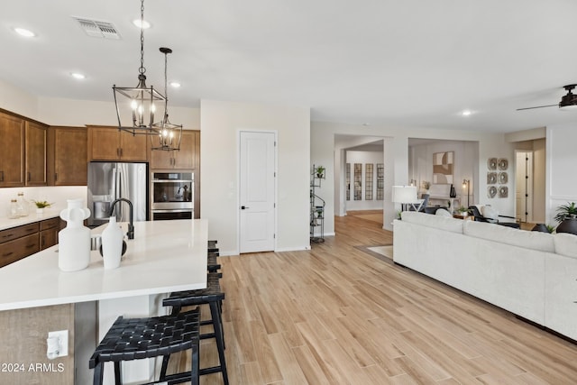 kitchen with a breakfast bar, decorative light fixtures, a center island with sink, appliances with stainless steel finishes, and light wood-type flooring