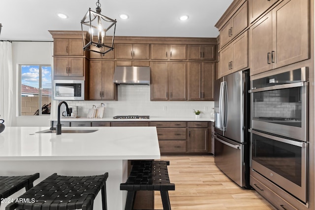 kitchen featuring pendant lighting, sink, range hood, appliances with stainless steel finishes, and light hardwood / wood-style floors