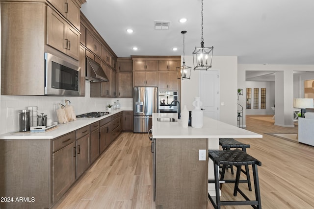 kitchen featuring light wood-type flooring, stainless steel appliances, a center island with sink, and sink