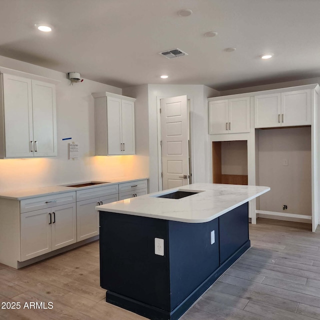 kitchen featuring a kitchen island with sink, light wood-type flooring, visible vents, and white cabinets