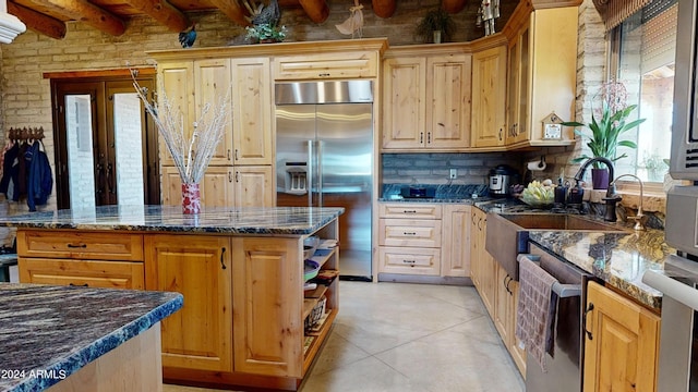 kitchen featuring stainless steel appliances, dark stone counters, beam ceiling, a kitchen island, and tasteful backsplash