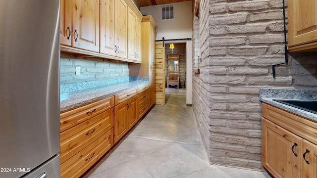 kitchen featuring a barn door, brick wall, light brown cabinetry, light stone countertops, and stainless steel fridge