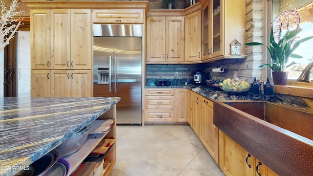 kitchen with sink, light tile floors, dark stone counters, built in fridge, and tasteful backsplash