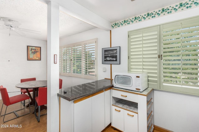 kitchen featuring beam ceiling, ceiling fan, wood-type flooring, a textured ceiling, and white cabinets