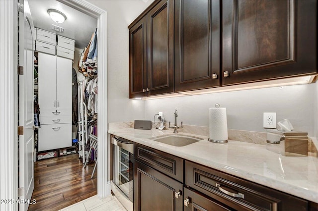 kitchen with sink, wine cooler, dark brown cabinetry, light stone countertops, and light hardwood / wood-style floors