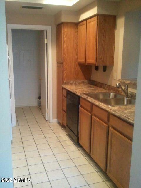 kitchen with light tile patterned flooring, black dishwasher, sink, and light stone countertops