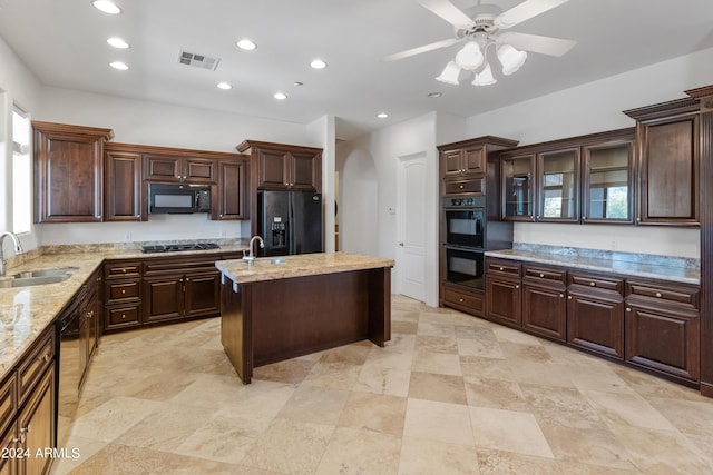 kitchen with sink, light stone counters, black appliances, dark brown cabinetry, and a kitchen island with sink