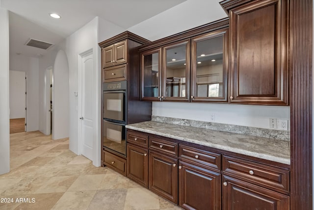 kitchen featuring dark brown cabinetry, light stone countertops, and black double oven