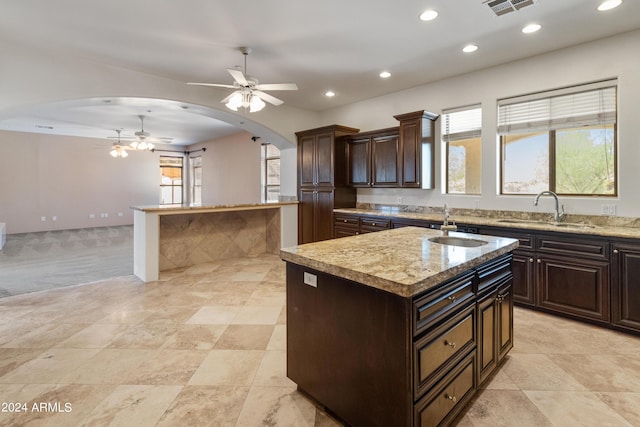 kitchen with a center island with sink, ceiling fan, sink, and dark brown cabinetry