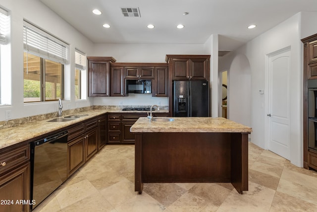 kitchen with dark brown cabinets, sink, an island with sink, and black appliances