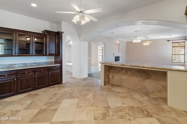 kitchen with ceiling fan, dark brown cabinetry, and light stone countertops