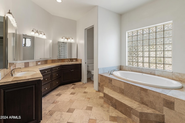 bathroom featuring toilet, vanity, tiled bath, and a healthy amount of sunlight