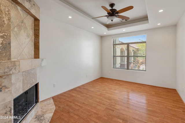 unfurnished living room featuring a raised ceiling, ceiling fan, light hardwood / wood-style flooring, and a premium fireplace