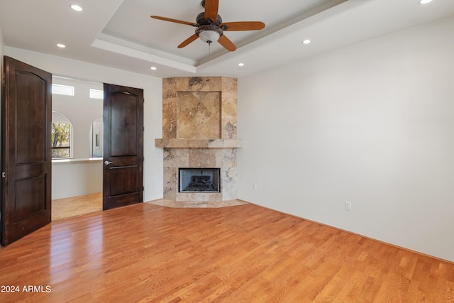 unfurnished living room featuring a tray ceiling, light hardwood / wood-style flooring, ceiling fan, and a fireplace