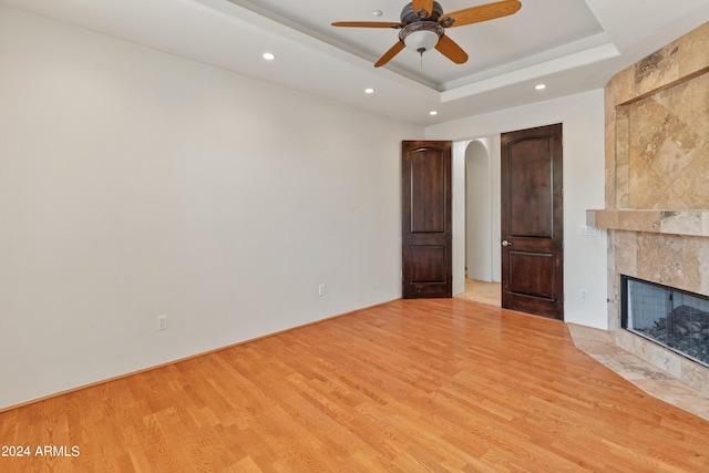 unfurnished living room with ceiling fan, light hardwood / wood-style floors, a tray ceiling, and a fireplace