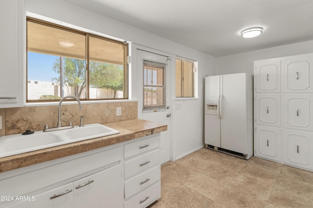 kitchen with white refrigerator with ice dispenser, white cabinetry, backsplash, and sink