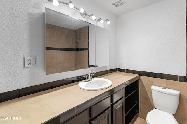 bathroom with tile walls, toilet, vanity, and a tile shower