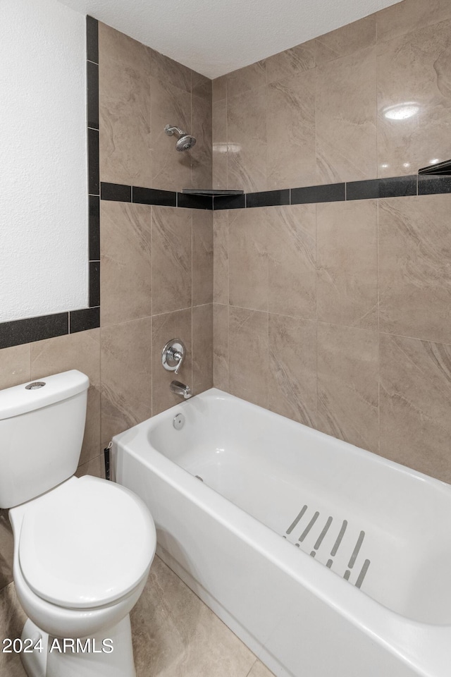 bathroom with tile walls, tiled shower / bath, and toilet