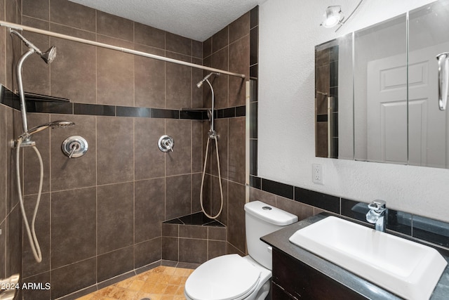 bathroom featuring a textured ceiling, a tile shower, vanity, and toilet