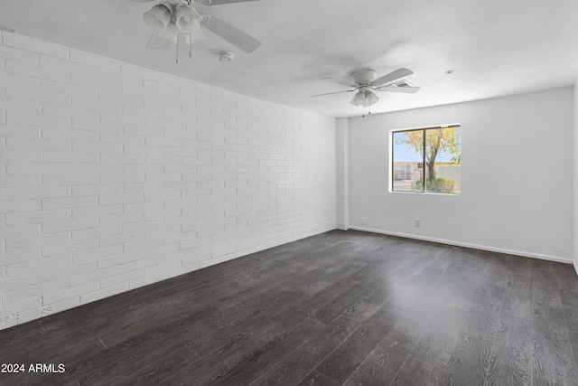 empty room with ceiling fan, dark wood-type flooring, and brick wall