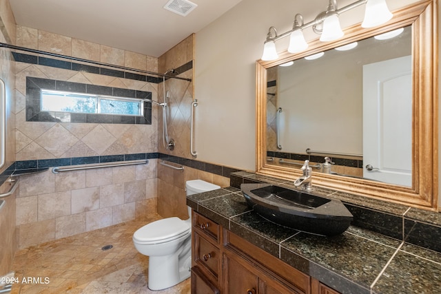 bathroom with tile walls, vanity, a tile shower, and toilet