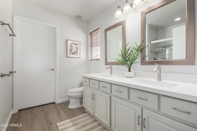 bathroom with wood finished floors, a shower stall, toilet, double vanity, and baseboards