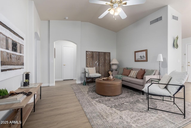 living room featuring arched walkways, a ceiling fan, lofted ceiling, light wood-style floors, and baseboards