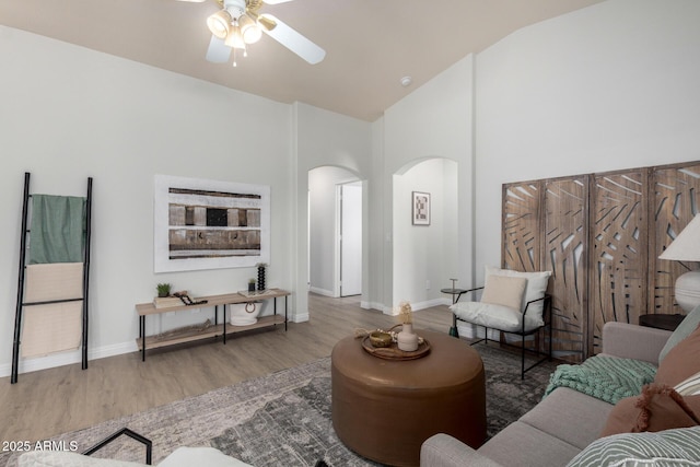 living area with arched walkways, wood finished floors, a ceiling fan, baseboards, and high vaulted ceiling