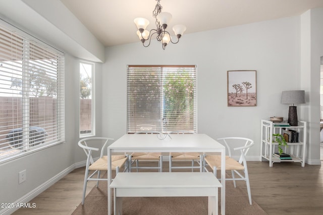 dining area featuring wood finished floors, a chandelier, baseboards, and lofted ceiling