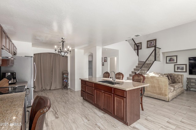 kitchen with a kitchen bar, light stone countertops, a kitchen island with sink, sink, and decorative light fixtures