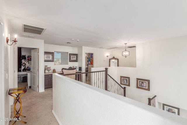 corridor with a notable chandelier and light colored carpet