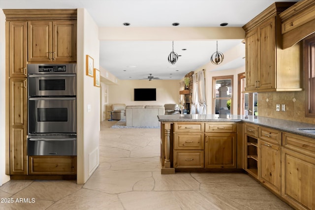 kitchen with kitchen peninsula, ceiling fan, pendant lighting, stainless steel double oven, and decorative backsplash