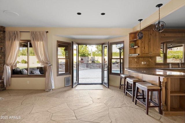 kitchen with kitchen peninsula, decorative light fixtures, a kitchen bar, decorative backsplash, and sink