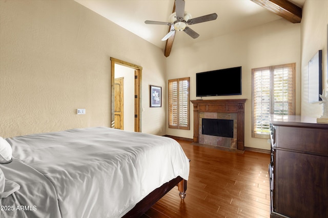 bedroom featuring ceiling fan, lofted ceiling with beams, a tiled fireplace, and dark hardwood / wood-style floors