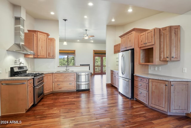 kitchen with appliances with stainless steel finishes, wall chimney exhaust hood, ceiling fan, dark wood-type flooring, and hanging light fixtures