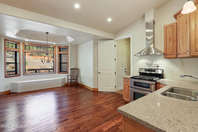 kitchen with dark hardwood / wood-style flooring, light stone counters, wall chimney exhaust hood, stainless steel gas range, and sink