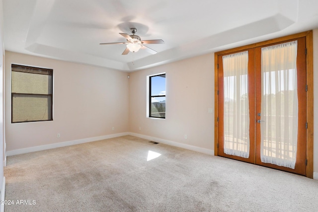 carpeted empty room featuring french doors, a tray ceiling, and ceiling fan