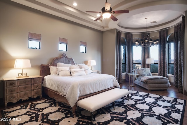 bedroom with wood-type flooring, ceiling fan with notable chandelier, and a raised ceiling