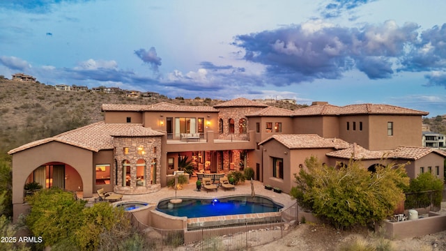 back of property featuring an in ground hot tub, a balcony, and a patio area